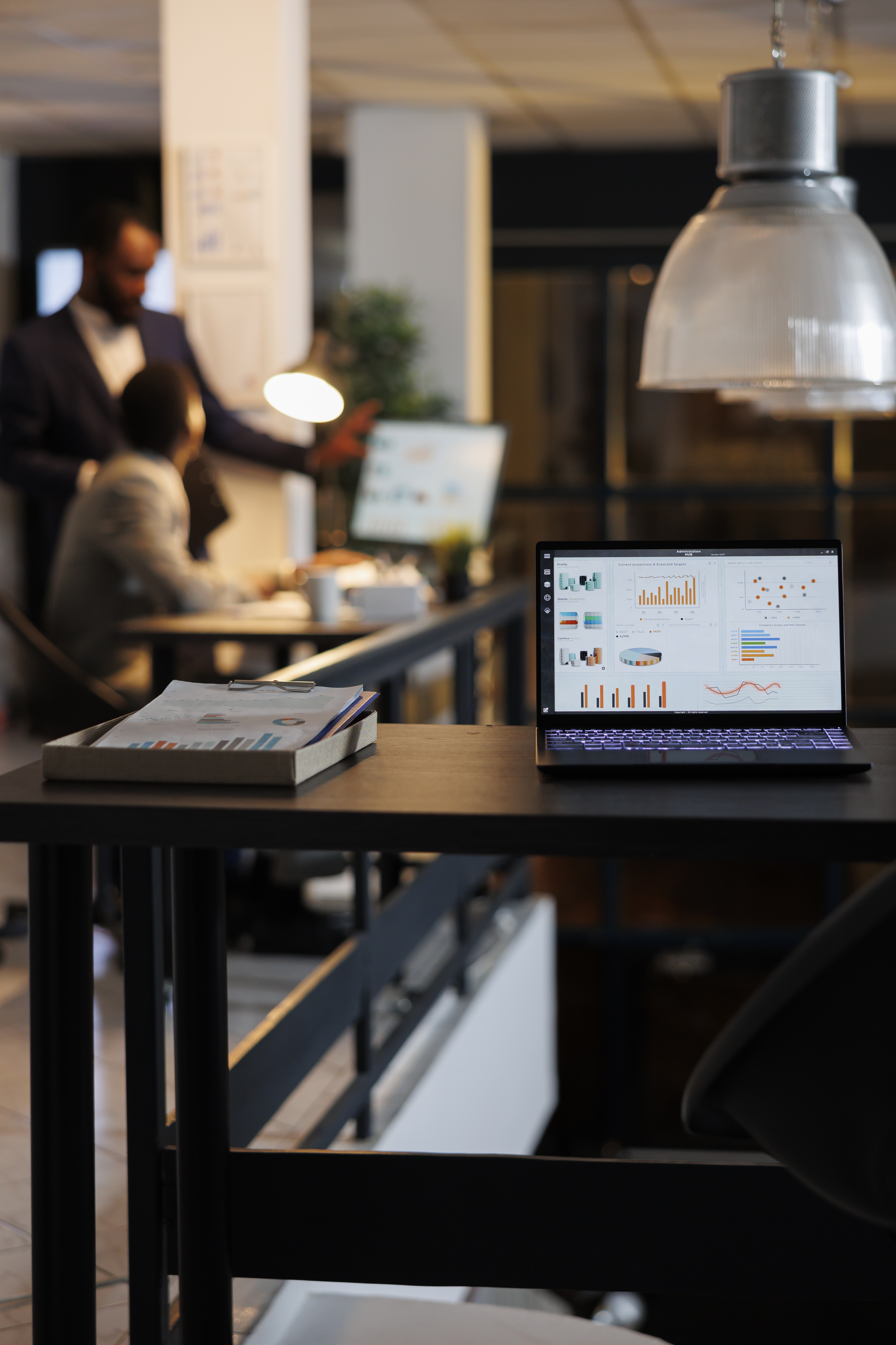 laptop-computer-with-financial-graphs-screen-standing-table-startup-office-coworkers-discussing-company-strategy-background-employees-working-late-night-startup-office.jpg